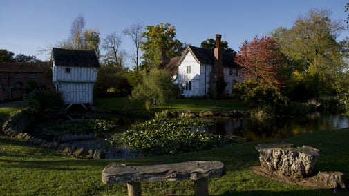 View across moat of two timber-framed houses with stone bench in foreground
